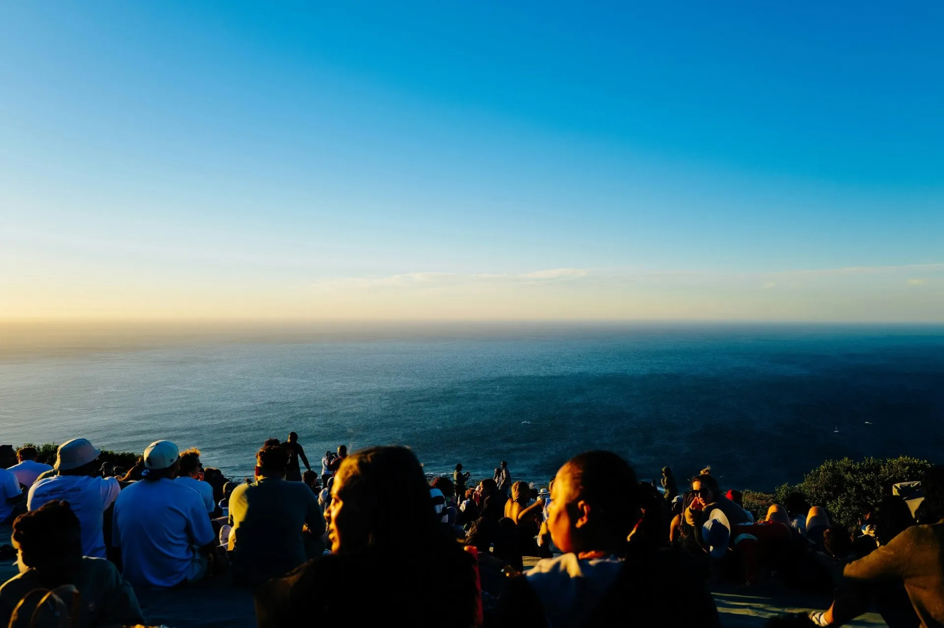 A crowd sitting on a hillside watching the sunset over the ocean